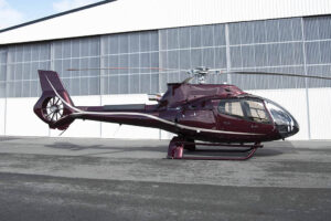 Maroon Gold Airbus EC130 T2 in front of Pacific Crown Helicopters hangar